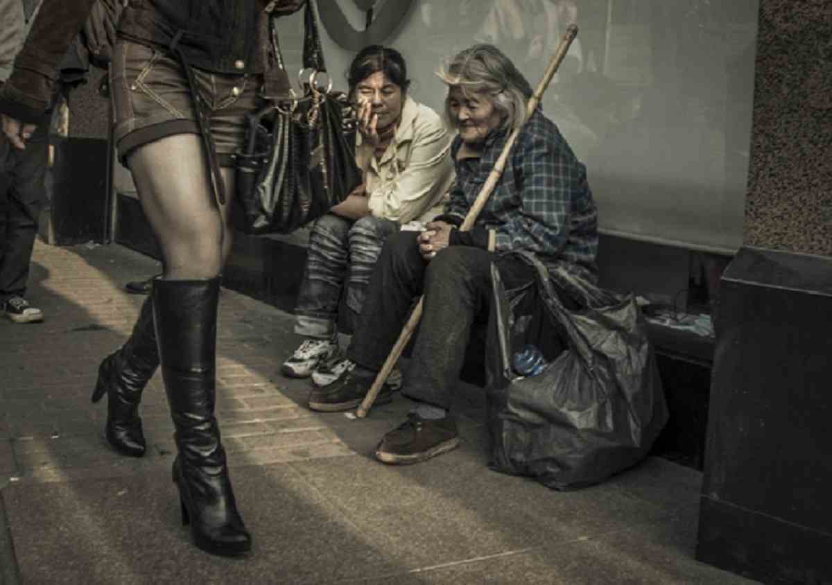 Famous street photography Ron Gessel captures a woman dressed in high fashion boots walking past two old beggars on The Street of Shanghai