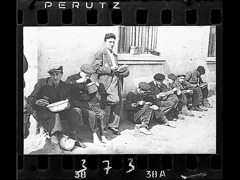 Image: Black and white photograph of Soup for Lunch, a group of men alongside building eating from pails,1940–44 by Jewish photographer Henryk Ross