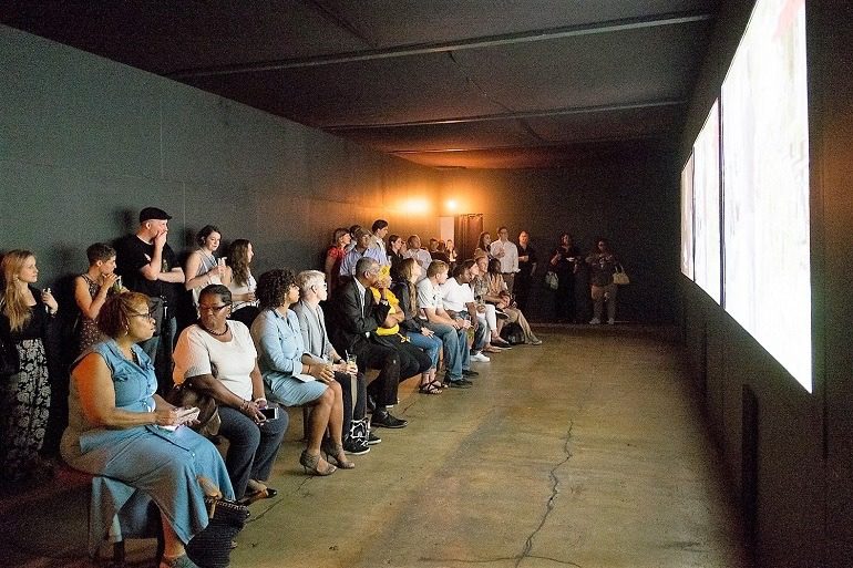 Image: At the VIP opening night of Darius Frank's Things I Loved in Washington DC, guests attentively viewed his multi-media exhibit