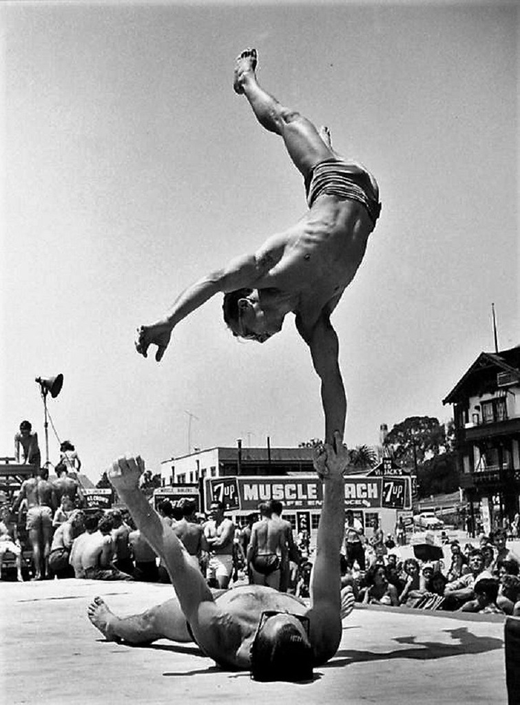 Image: A black and white photograph of Two Men Doing a Handstand, Muscle Beach, Santa Monica, CA, 1954 by Larry Silver