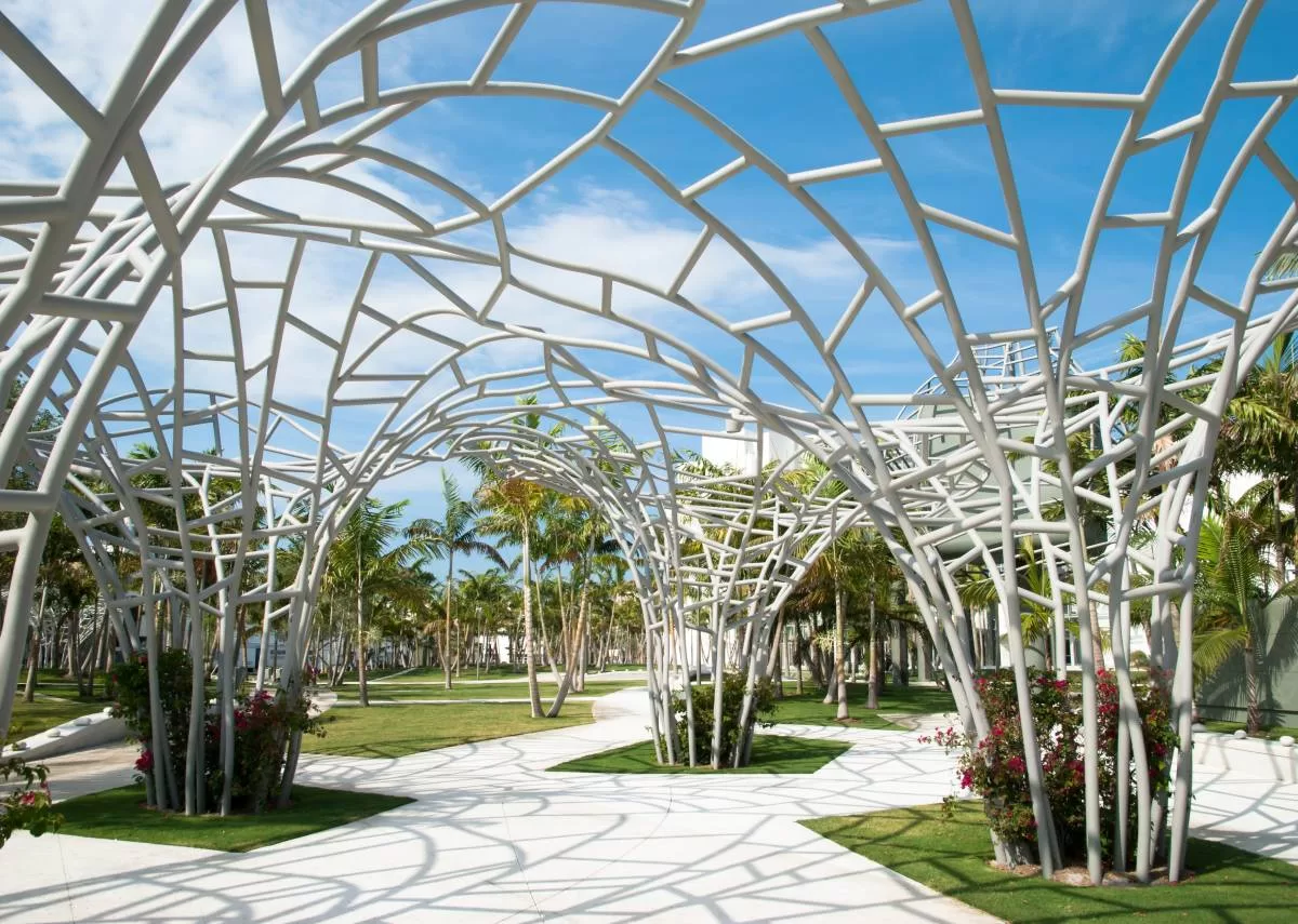 A modern park filled with green spaces, palm trees, and abstract public art installations scattered throughout the area.