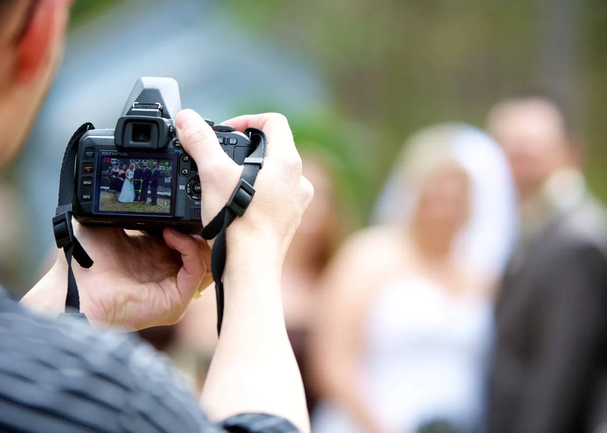 A photographer looks at a small wedding party through the display of his handheld camera, preparing to take the photo.