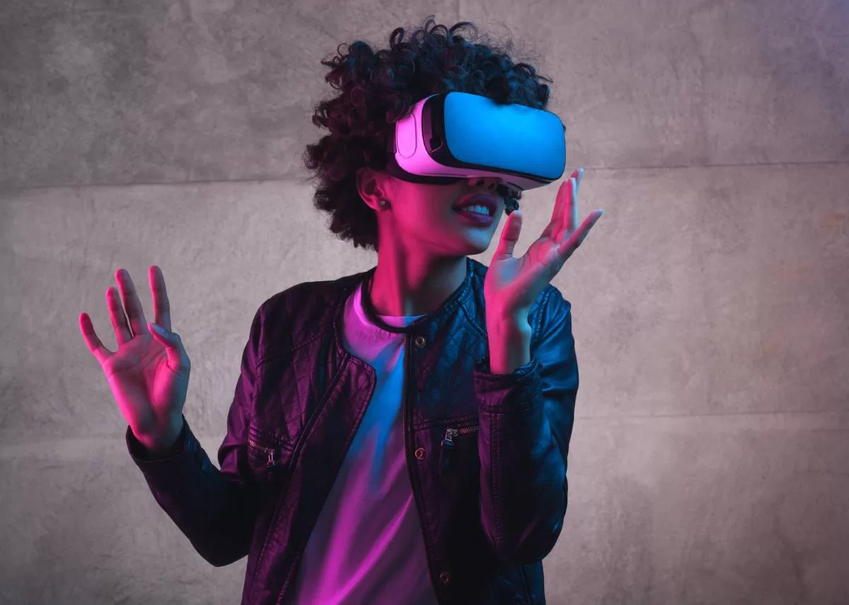 A young woman with curly hair wears a virtual reality headset. She holds her hands out as if interacting with an environment. The question remains, how virtual reality transforms the moviegoing experience