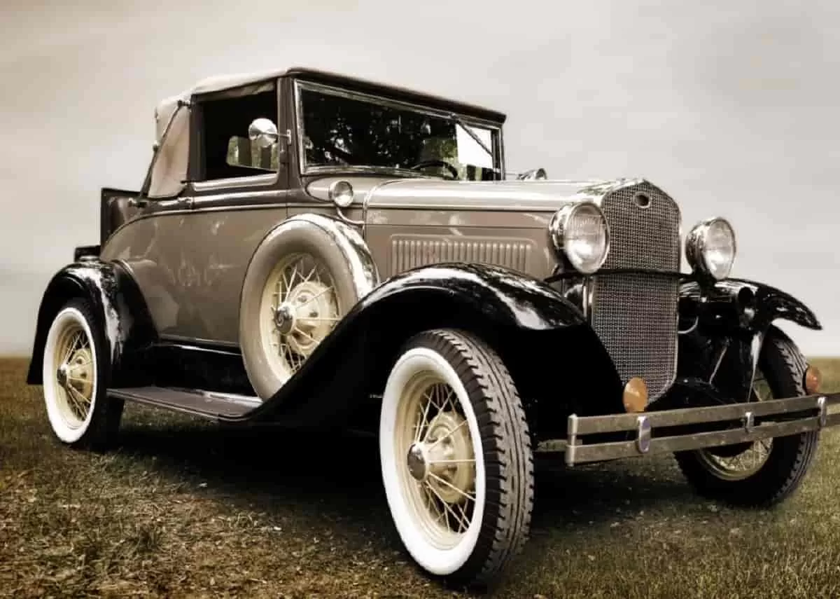 A old, classic car with a shiny bronze coat is parked in the middle of a field with an overcast of clouds overhead. Learn about the art and design behind classic cars like this.