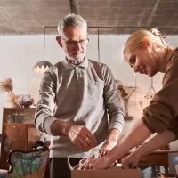 A young woman helps a well-groomed older man pack expensive pieces of art into a brown cardboard box. Such attention to detail is important when shipping heavy artwork