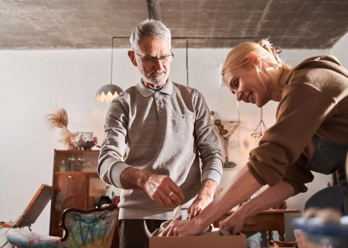 A young woman helps a well-groomed older man pack expensive pieces of art into a brown cardboard box. Such attention to detail is important when shipping heavy artwork