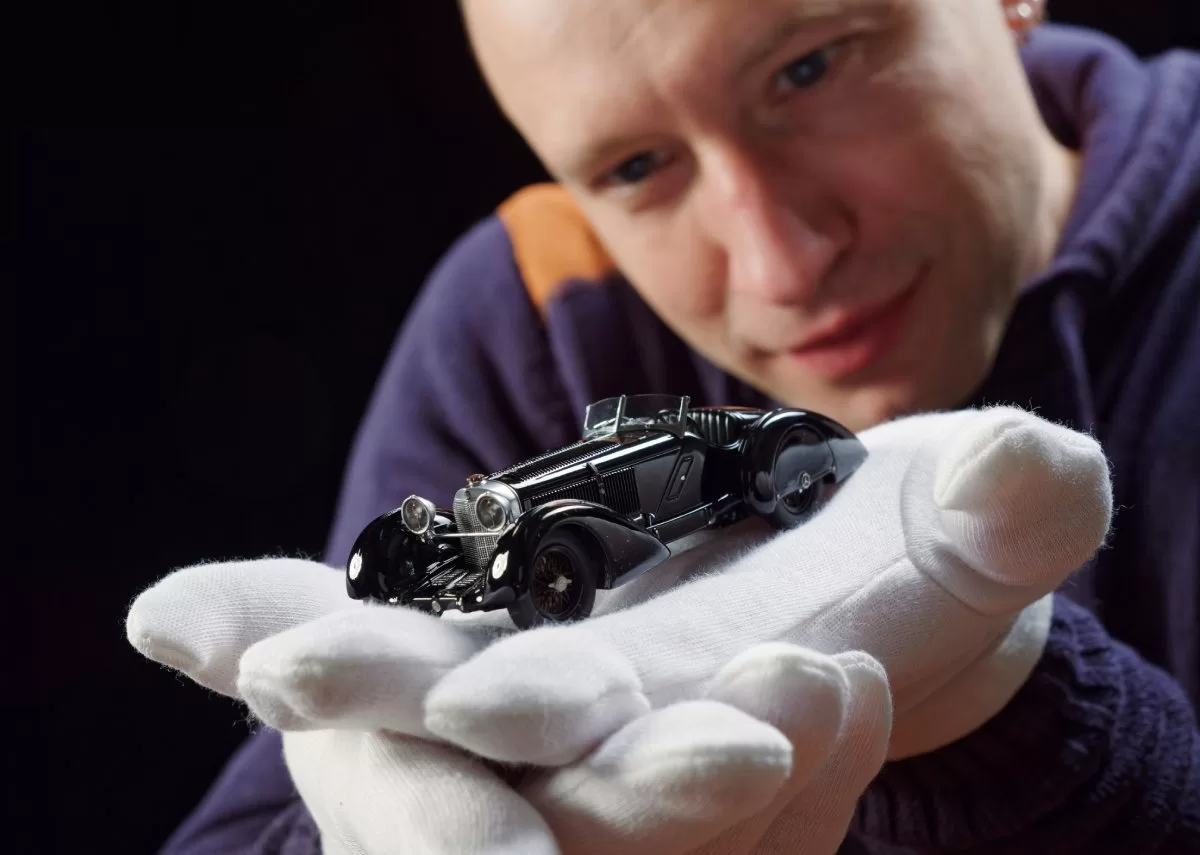 A collector wears white gloves and holds a vintage diecast car model, showcasing its intricate details and craftsmanship. Curating diecast collections for art dealers requires historical knowledge and understanding of design.