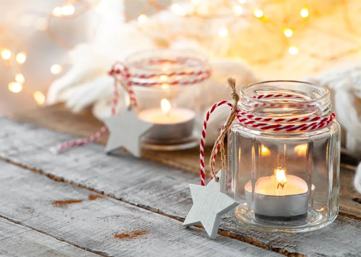 A table decorated for the holidays with glass candle holders and tealight candles lit inside. There's a red and white ribbon. Elevate your festive vibe with glass holiday decorations