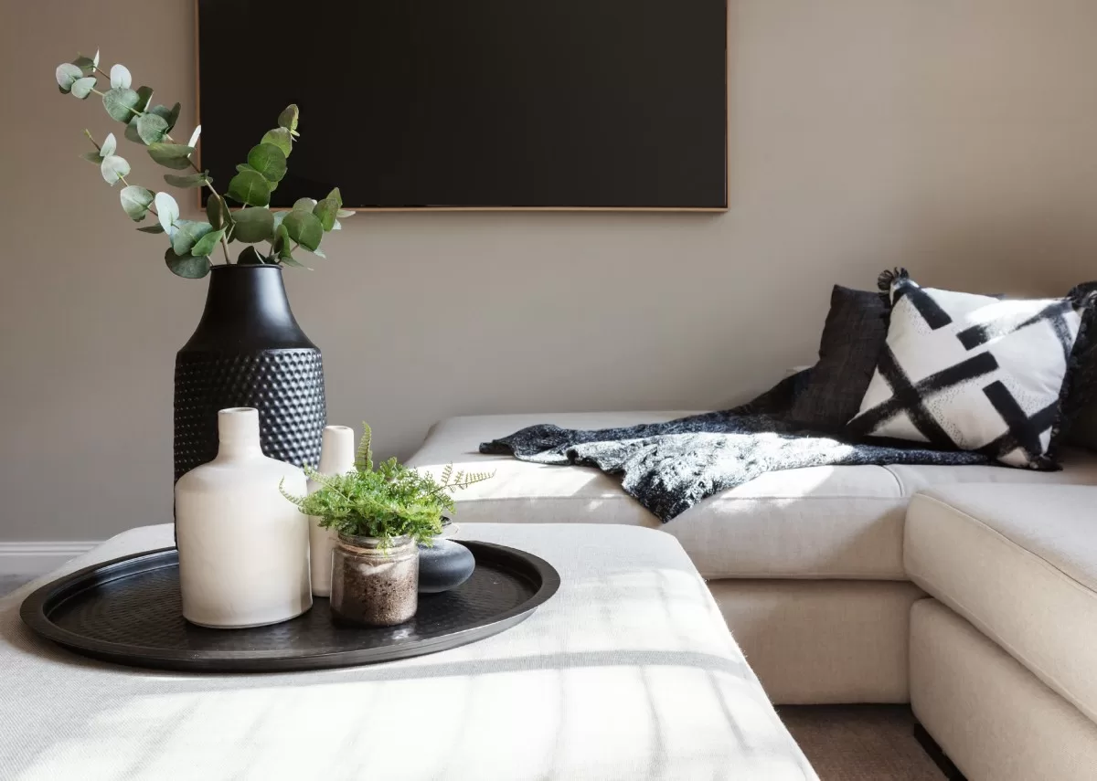 A creme-colored sectional with the same colored footstool in the middle. A pillow, blanket, and vases are used as decor. Great example of budget-friendly decor hacks for a luxurious home.