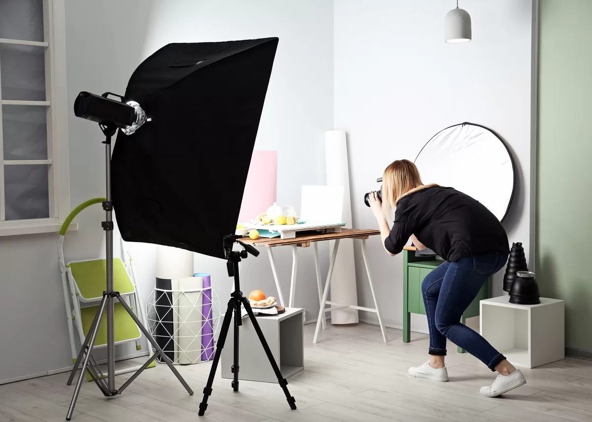 A woman takes photos of food in a basement photography studio. Lighting equipment and backdrops are nearby. Setting up a photography studio is one of the creative uses for your basement