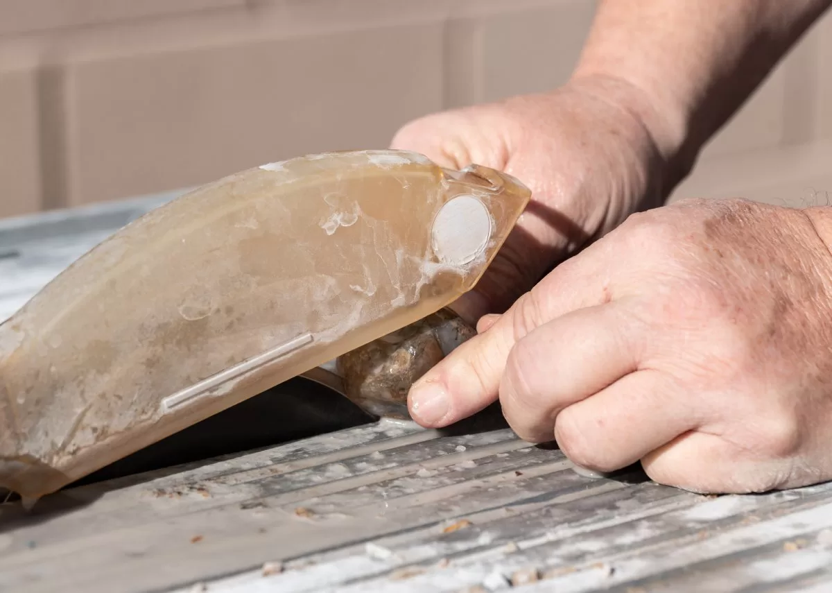 A person holds a large gemstone on the flat surface of a lapidary slab saw, which begins to cut the material.