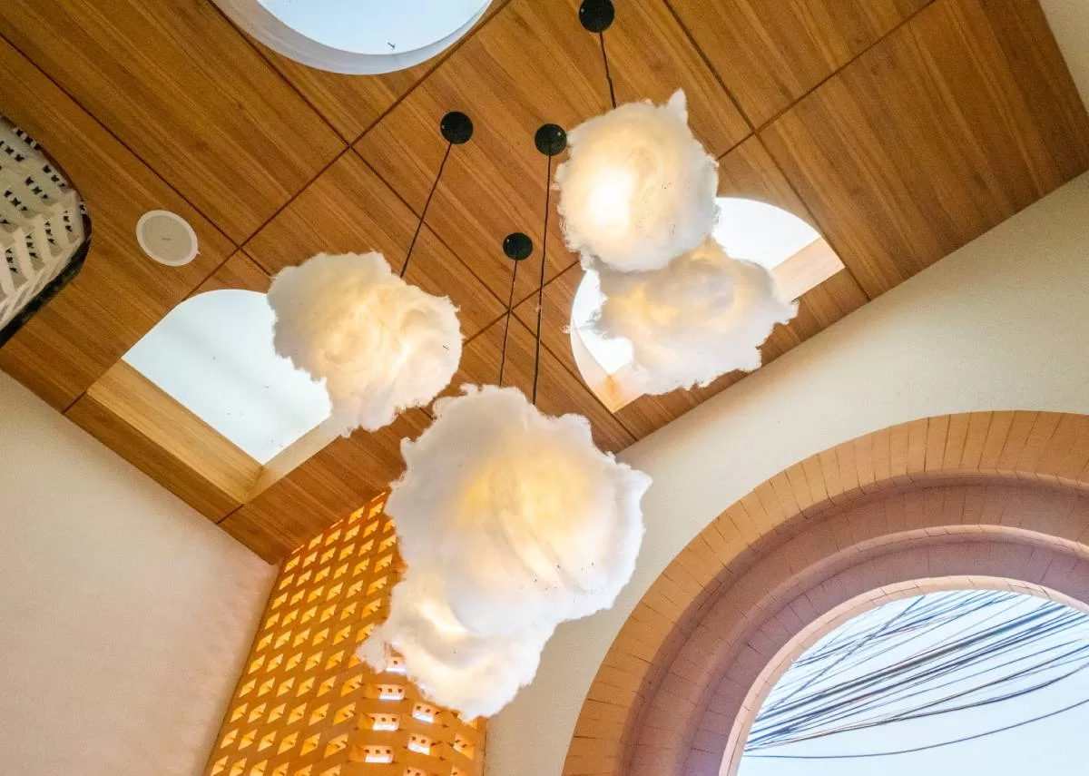 An upward view of the ceiling lights in a dining room. The lights have a cloud-like texture and the ceiling is made of wood.