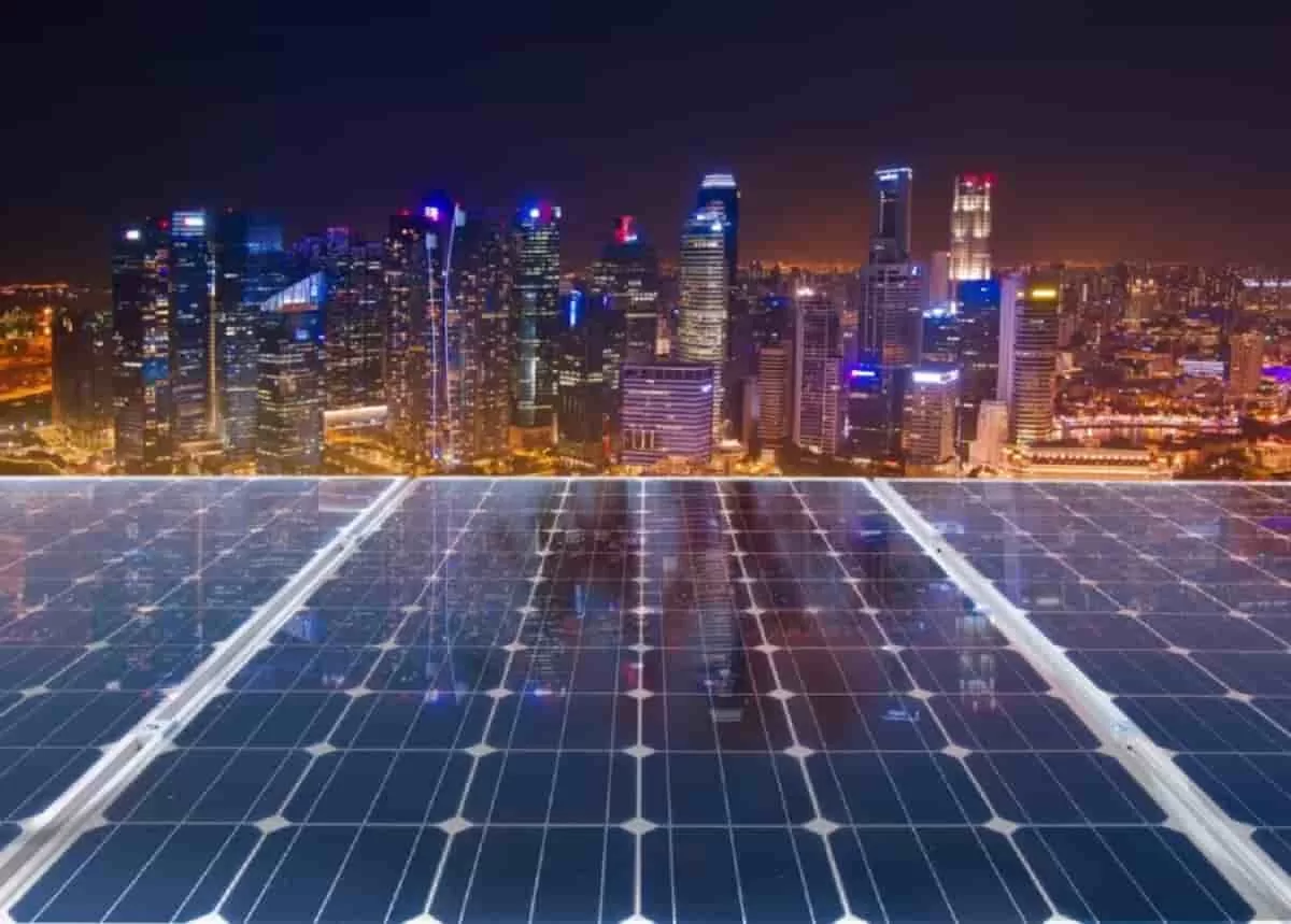 A close-up of solar panels powers a building at night, with a modern city skyline in the background.