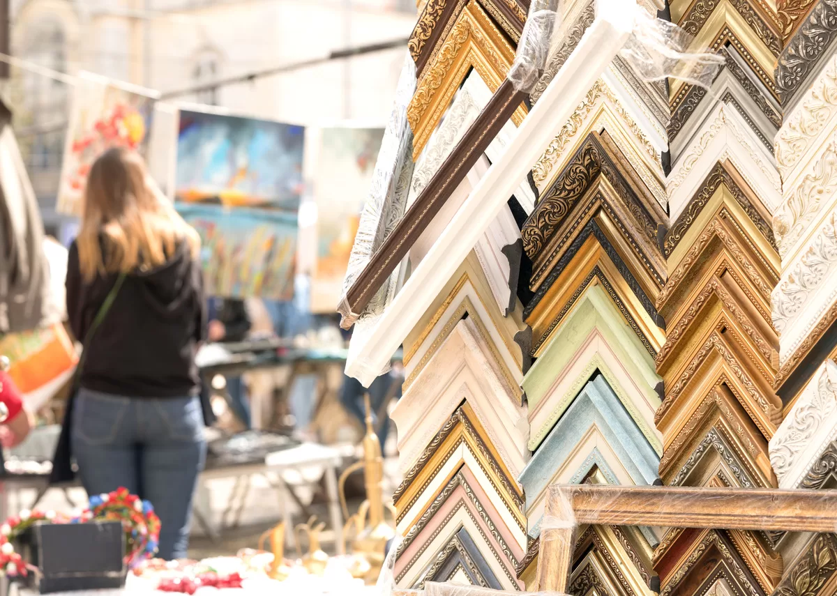 Rows of wooden and plastic picture frames, up close and in different colors and sizes. Behind them are some canvas art. It is important to learn how to create custom framing for your artwork.