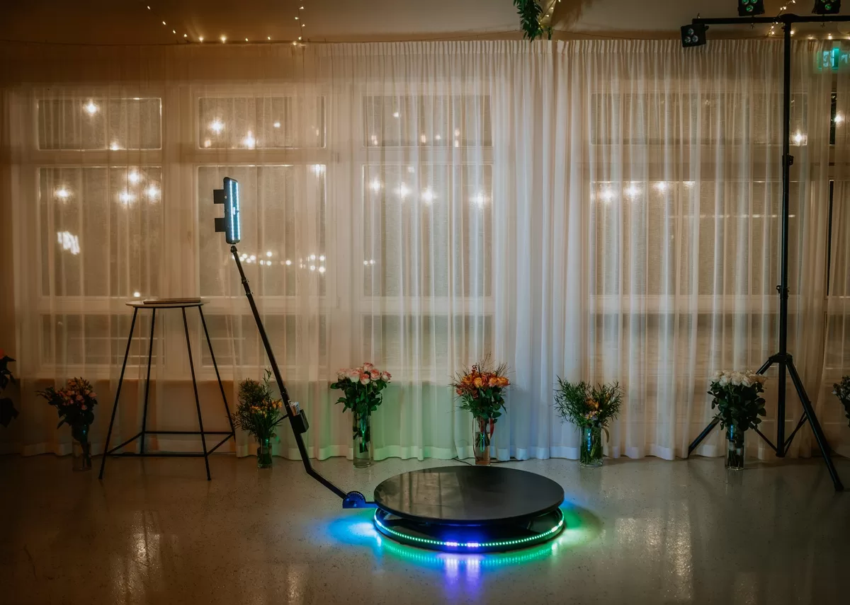 A 360-degree photo booth setup with LED lights and a round, rotating platform is surrounded by floral arrangements. With such setup, the impact of photo booths on social media engagement can be elevated.