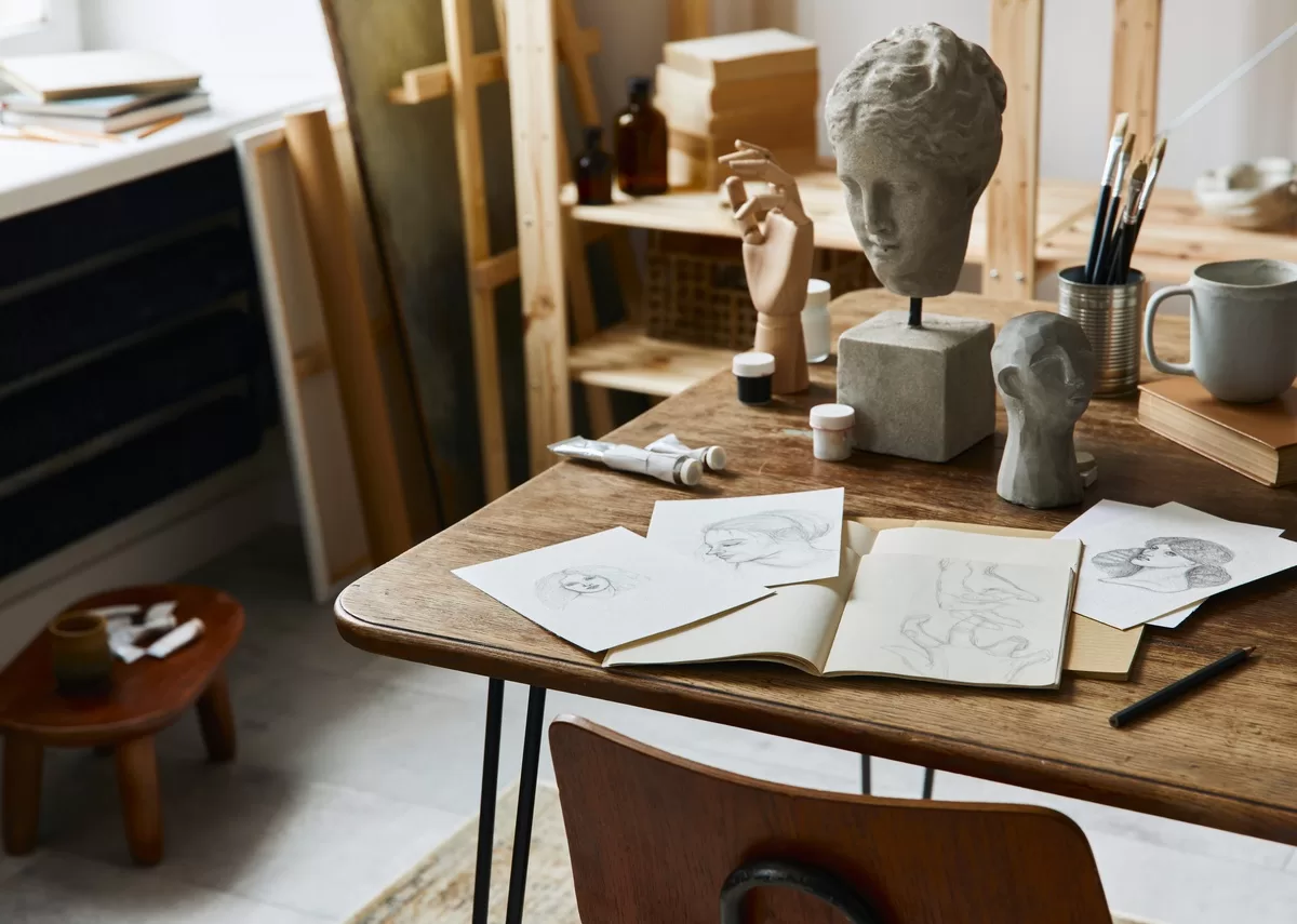 An artist's workspace features a wooden easel, a desk, and shelves stocked with books, paintings, and creative tools. These are examples of how artists are using 3D printing in the art and design industry.