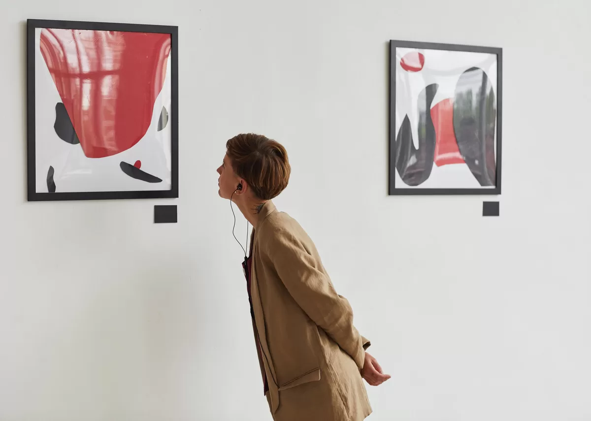 A young woman in an art museum. She wears earbuds and leans forward to examine an abstract painting. It is important to avoid the misconceptions about modern art when you go to art exhibitions