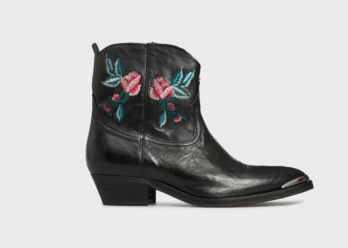 A short black boot with embroidered flowers in blue and pink with a silver toe tip sits against a white background. The boot exemplifies the rise of handcrafted details in fashion design is reshaping demands for handcrafted fashion.