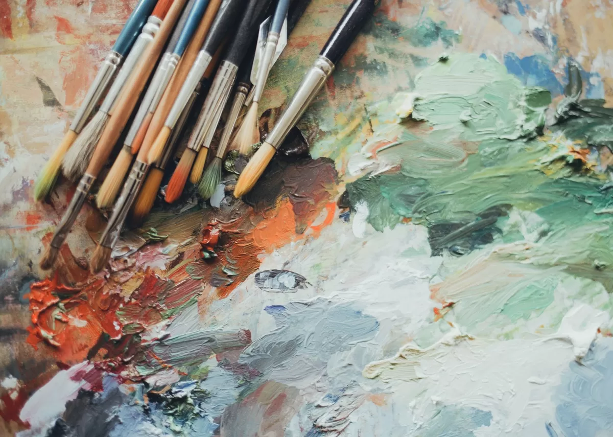 Paintbrushes rest on a colorful canvas that has been painted with broad, layered strokes of different colors. Colors are major inspiration for famous artworks inspired by timeless classic novels