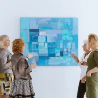 A group of four mature women is gathered around a blue contemporary abstract painting at an art show.