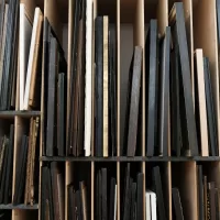 Storage shelves with assorted framed artworks and canvases organized vertically in narrow wooden rack compartments. A good gallery storage and organization will protect your art.