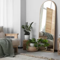 A living room with a tan futon and green blanket. Several plants rest on baskets, with a tall mirror resting against a wall. Plants and mirrors are design choices that make homes feel more spacious