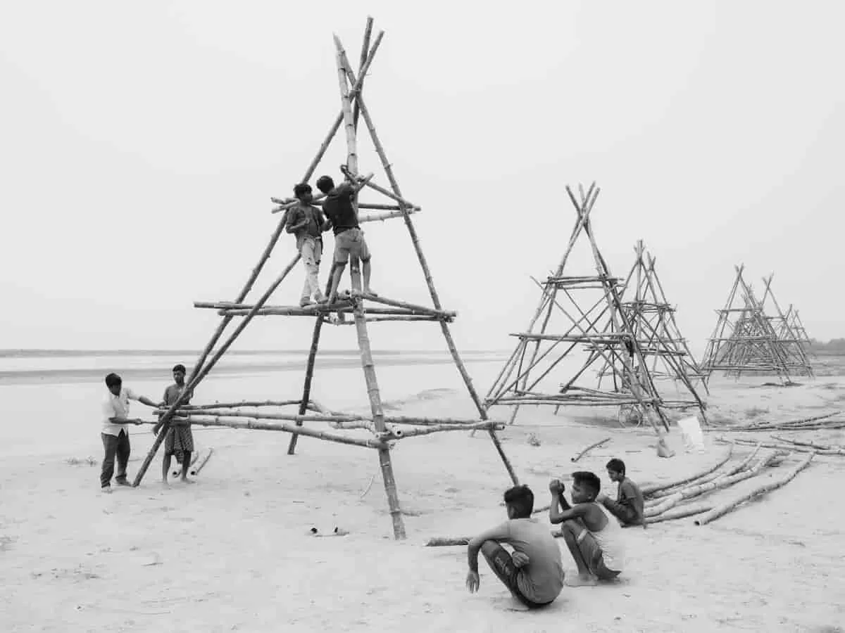 Black and white photograph titled The Edge by Zishaan A Latif showing Miya young men building a bamboo scaffolding structure to prevent erosion along the Brahmaputra River.