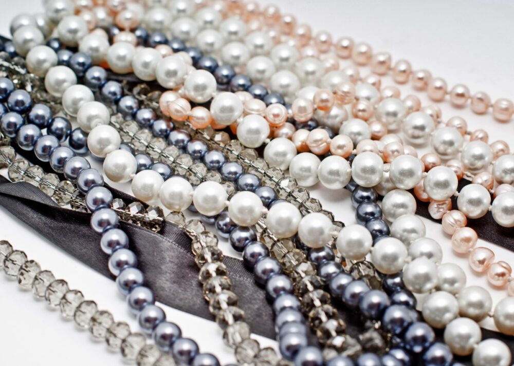 A group of pearl necklace strands with different pearl sizes and colors arranged in loose overlapping loops.