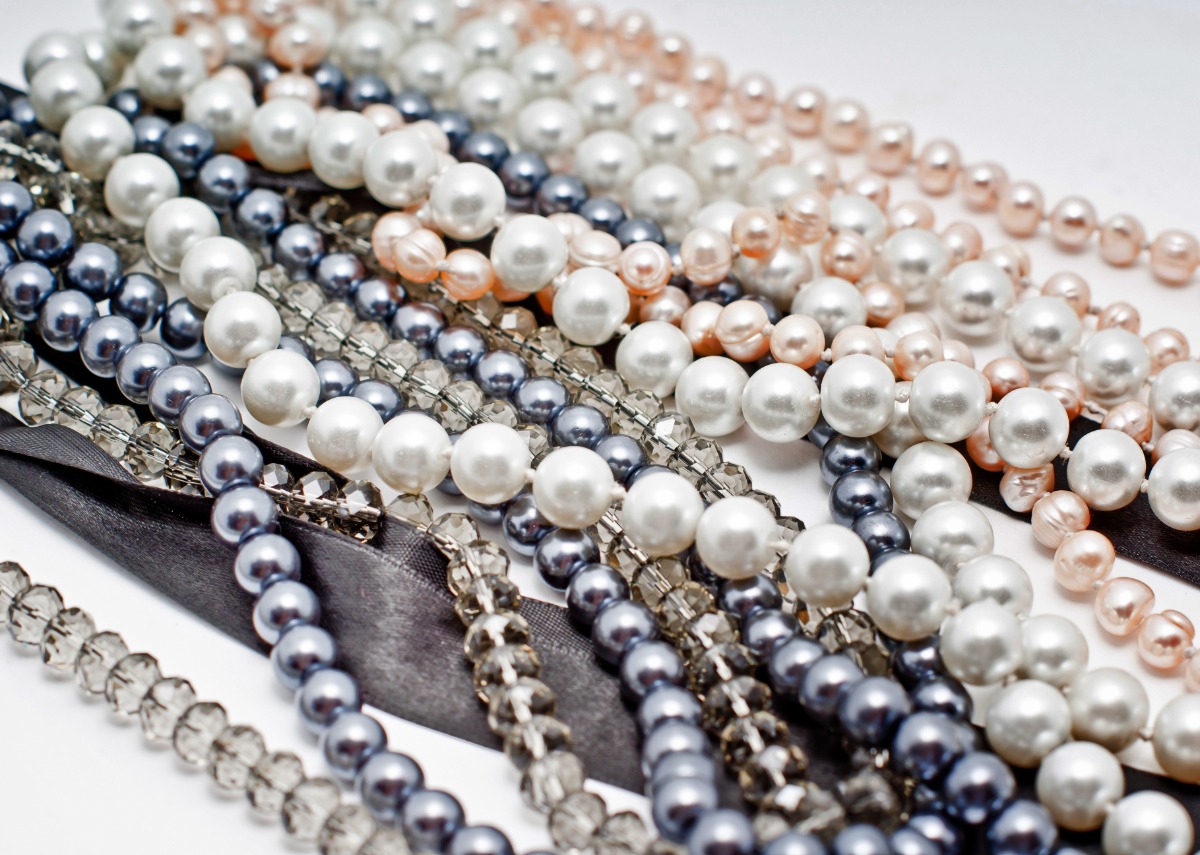 A group of pearl necklace strands with different pearl sizes and colors arranged in loose overlapping loops.