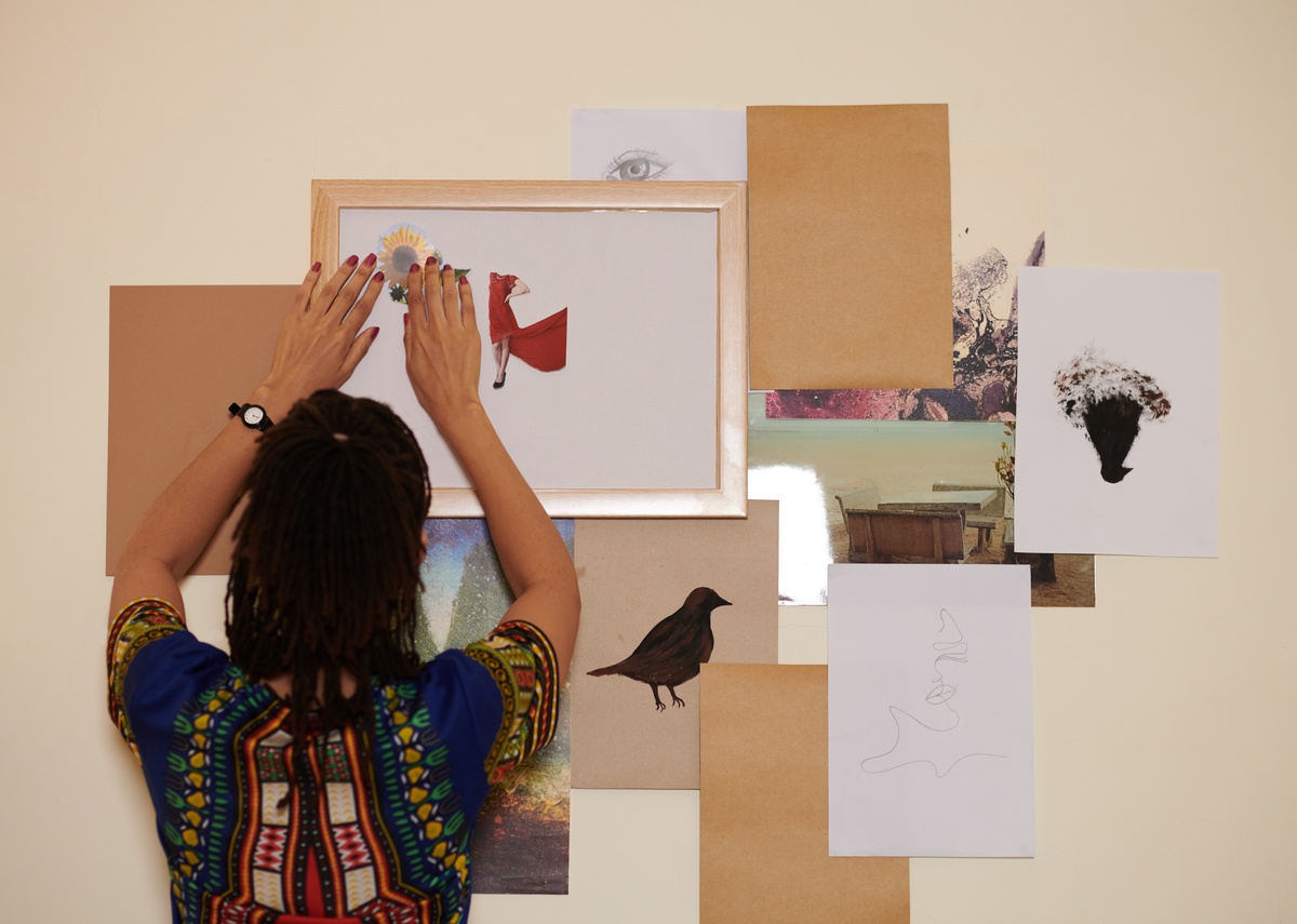 a woman arranging cutout photos on a white sheet inside a frame while creating a creative moodboard on the wall.