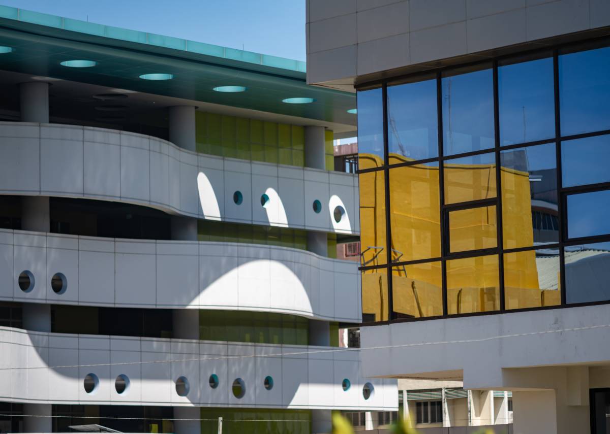 Contemporary architecture with white curved walkways, circular openings, and mirrored glass reflecting yellow walls.