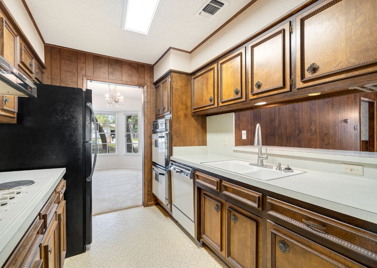 An outdated kitchen with older appliances. The cabinets have unique vintage knobs and trim along the panel.