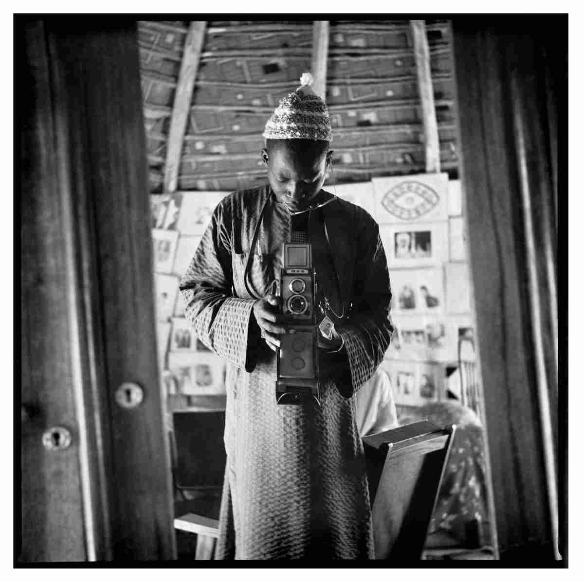 Here are SEO-friendly versions that incorporate the primary keyword **"Baltimore Museum of Art acquisitions"** naturally. ### Alt Tag **Baltimore Museum of Art acquisitions: Photographer Oumar Ka takes a self-portrait holding a vintage camera while wearing a Sufi hat honoring Senegalese Saint Amadou Bamba, with dozens of studio portraits displayed behind him.** ### Caption 1 As part of the **Baltimore Museum of Art acquisitions**, photographer Oumar Ka presents a self-portrait holding a vintage camera. Wearing a hat identifying him as a follower of the Senegalese Sufi saint Amadou Bamba, he stands before dozens of portraits that reflect his artistic identity. ### Caption 2 Featured in the **Baltimore Museum of Art acquisitions**, this self-portrait by Oumar Ka shows the artist holding a vintage camera while wearing a hat associated with followers of Senegalese Saint Amadou Bamba. The portraits filling his studio backdrop underscore his creative persona. ### Caption 3 The **Baltimore Museum of Art acquisitions** include this striking self-portrait by Oumar Ka, who poses with a vintage camera and a hat signifying his devotion to the Senegalese Sufi saint Amadou Bamba. A wall of portraits behind him reinforces his role as both photographer and subject. ### Description Among the **Baltimore Museum of Art acquisitions**, Oumar Ka's self-portrait offers an intimate view of the artist's identity and practice. Holding a vintage camera, Ka wears a hat identifying him as a follower of the Senegalese Sufi saint Amadou Bamba. Behind him, dozens of portraits displayed throughout his studio create a layered backdrop that reflects both his prolific body of work and his carefully constructed artistic persona. The composition intertwines photography, spirituality, and self-representation, highlighting Ka's distinctive approach to portraiture.