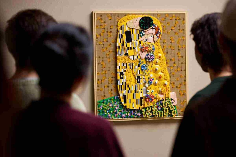 Some art lovers admire the completed LEGO Gustav Klimt The Kiss Set hanging on a wall as a decorative art display.